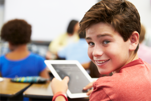 Young boy in a classroom pressing down on a tablet device